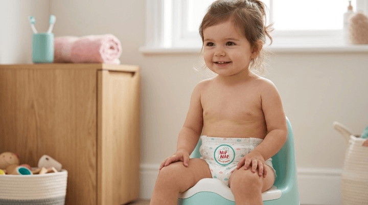 Toddler wearing potty training pants Kenya parents use, sitting on a child's potty seat