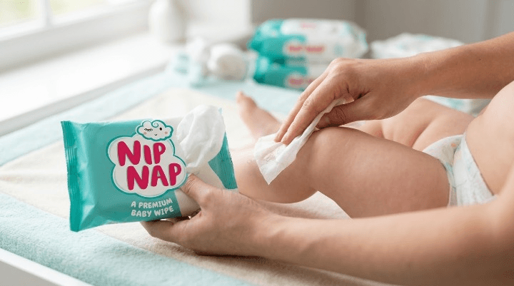 Mother gently cleaning her baby's nappy area with a soft baby wipe on a changing mat