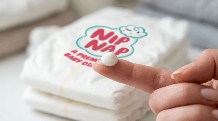 Close-up of a parent's fingertip with a small amount of barrier cream beside a folded clean nappy